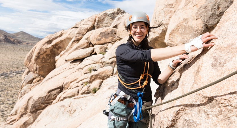 a student in rock climbing gear smiles at the camera amongst tan rocks